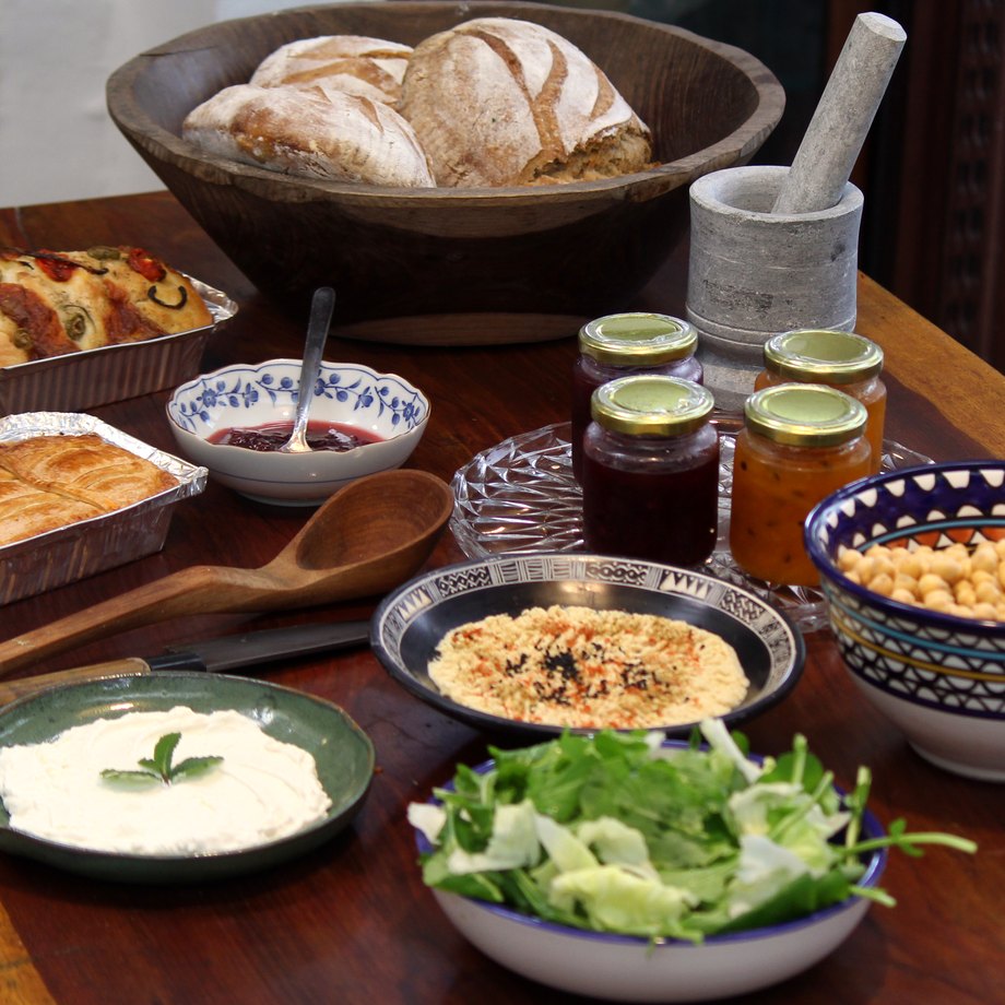Mesa farta com pães, focaccia, torta, geleias, homus e coalhada