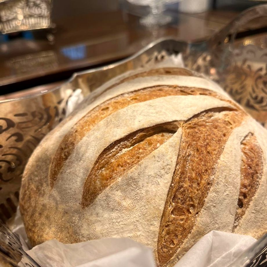 Pão de fermentação natural com pestana dourada, servido numa cesta prateada